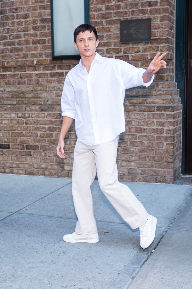 a man in a white shirt and white pants is standing in front of a brick building