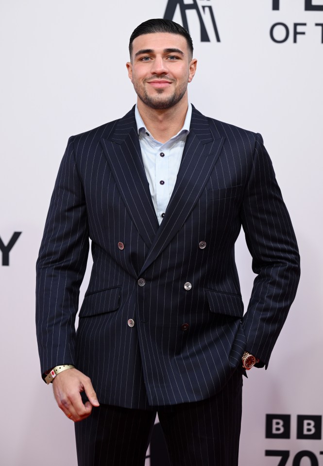 a man in a suit stands in front of a bbc logo