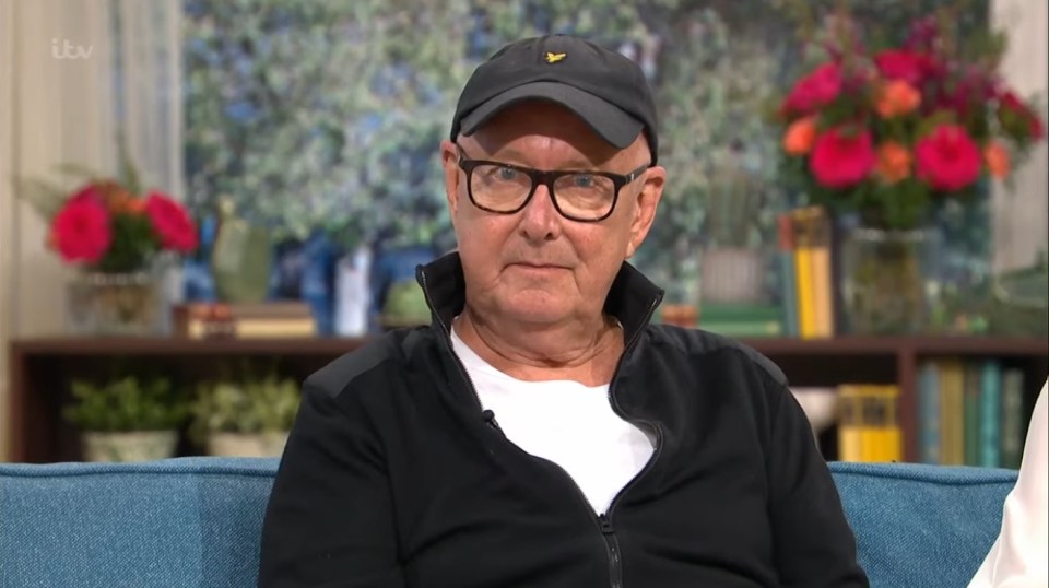 an older man wearing a hat and glasses sits on a couch