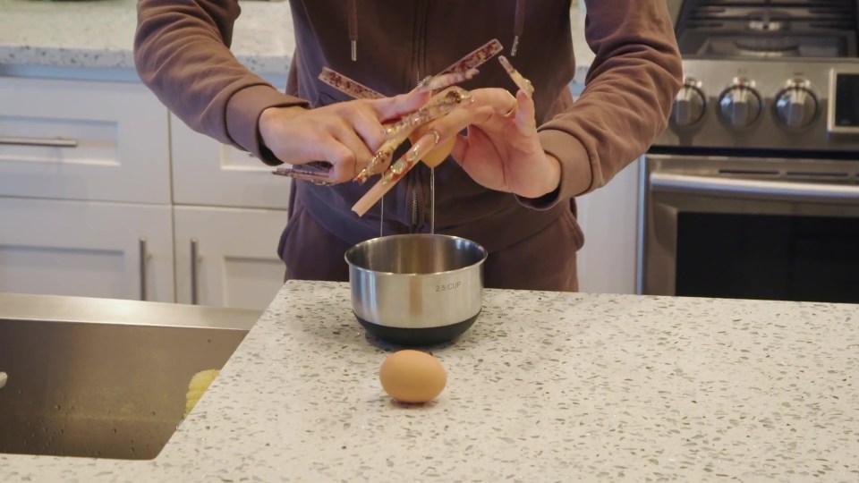 a person in a brown sweatshirt is holding a tong over an egg