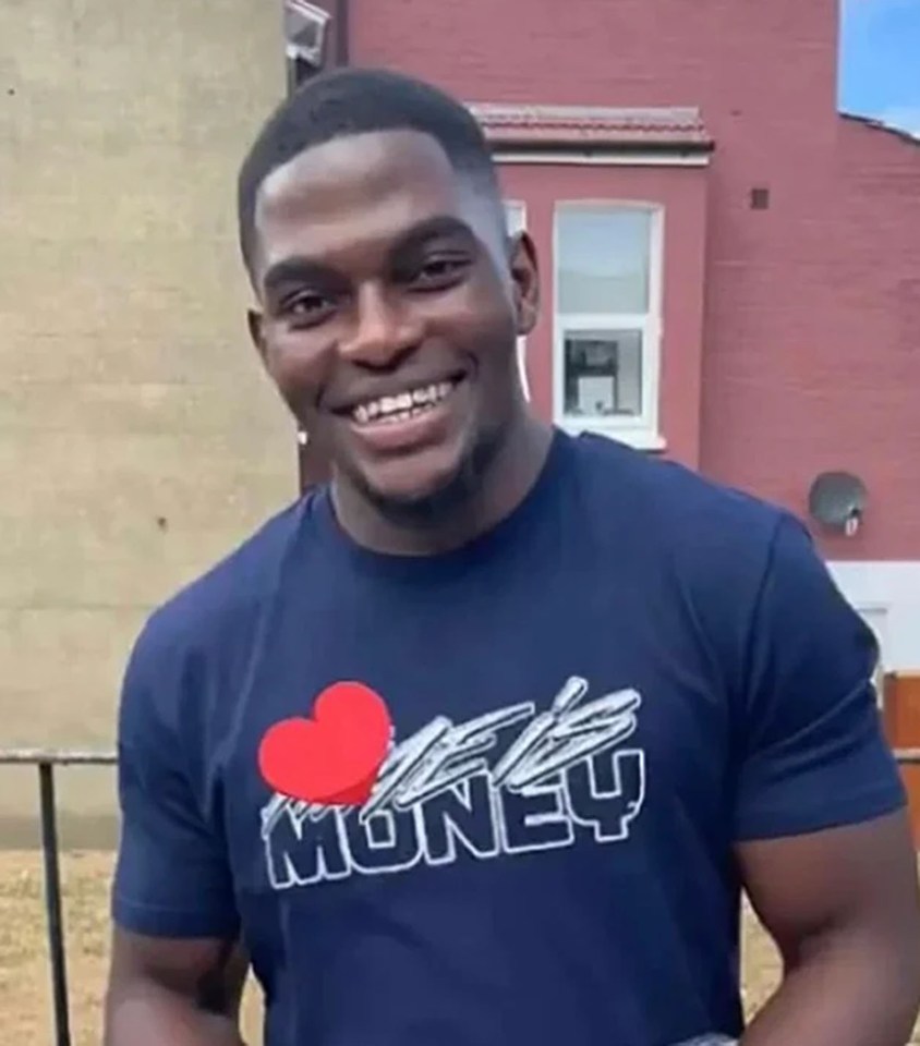 a man wearing a t-shirt that says `` i love money '' is smiling in front of a red building .