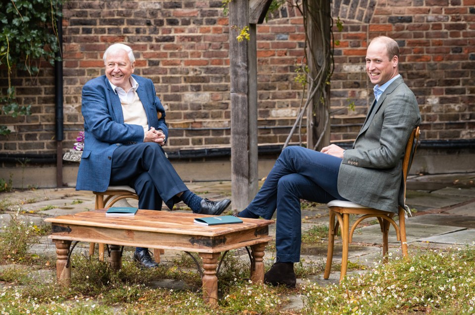 a man in a suit sits next to another man in a chair