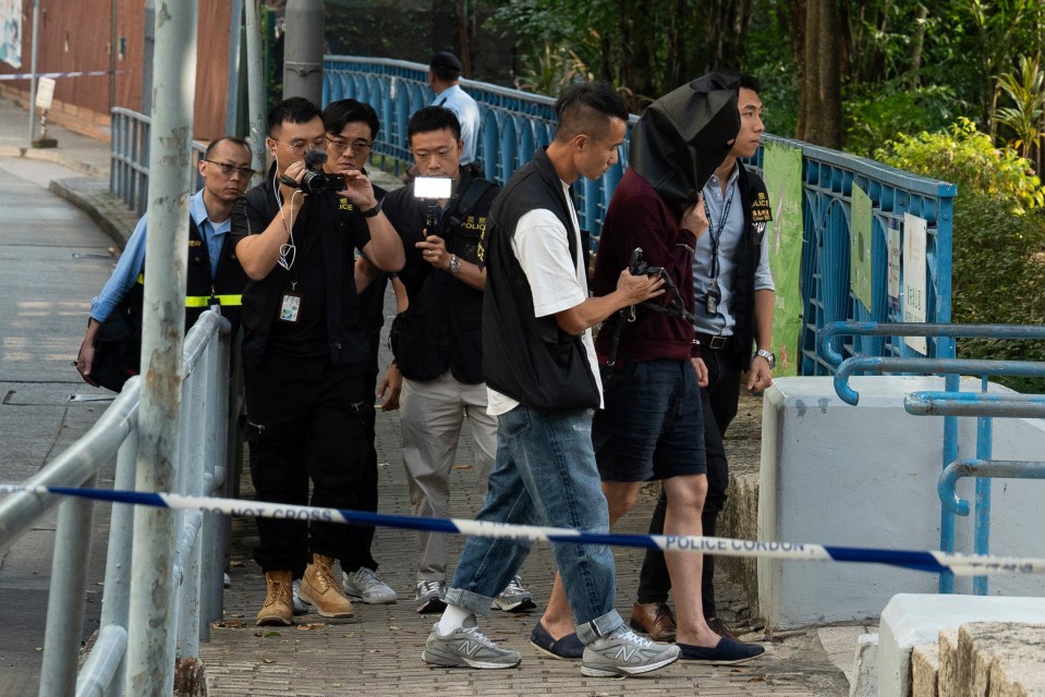 An unidentified person, possibly the wife, is escorted away by police with a hood on