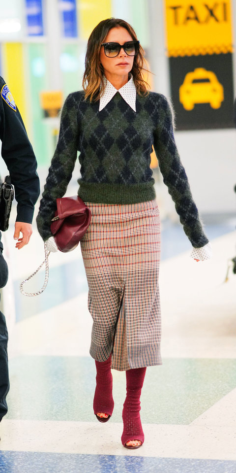 a woman wearing a sweater and plaid skirt is walking in front of a taxi sign