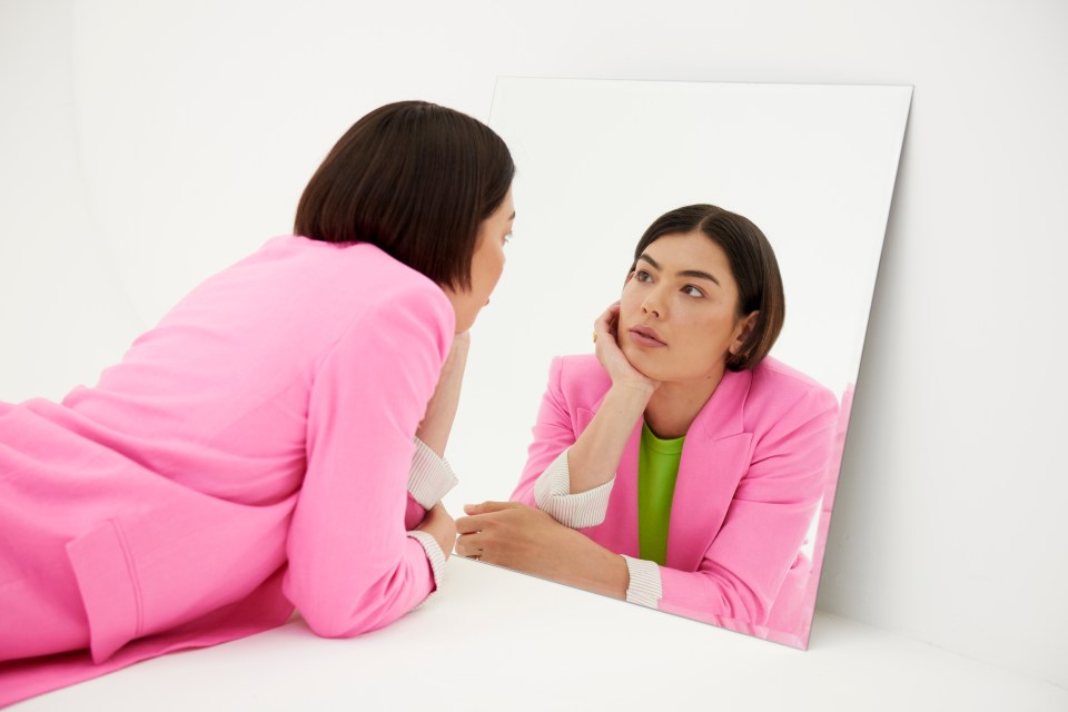 a woman in a pink suit looks at her reflection in a mirror