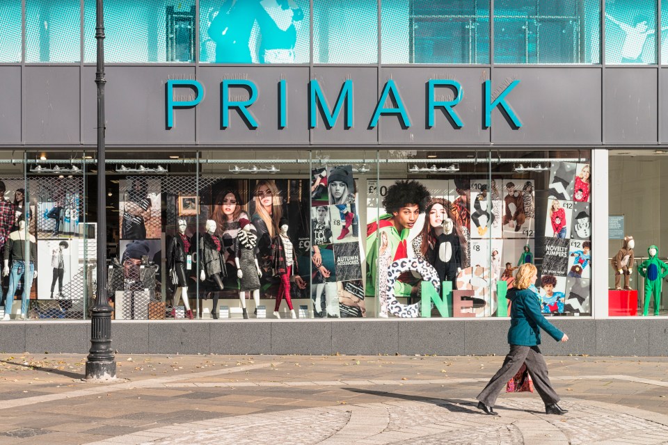 a woman crosses the street in front of a primark store