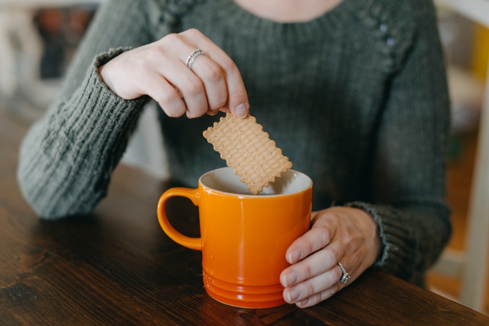 a woman takes a cookie out of an orange mug