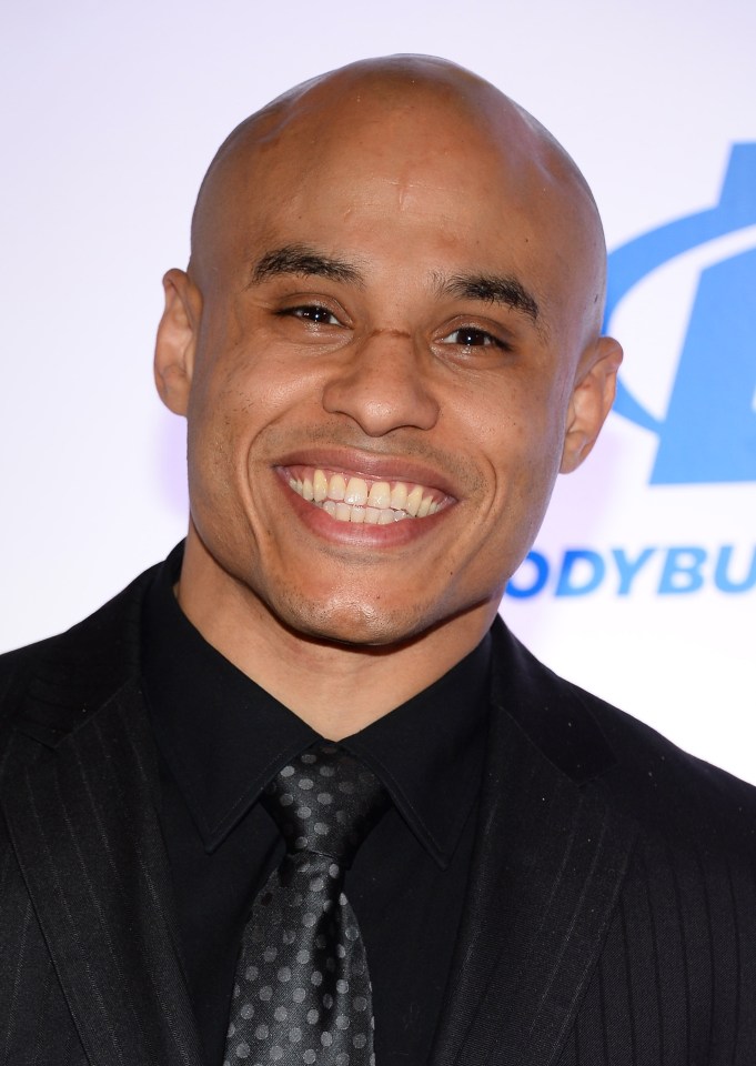 a man in a suit and tie smiles in front of a bodybuilder logo