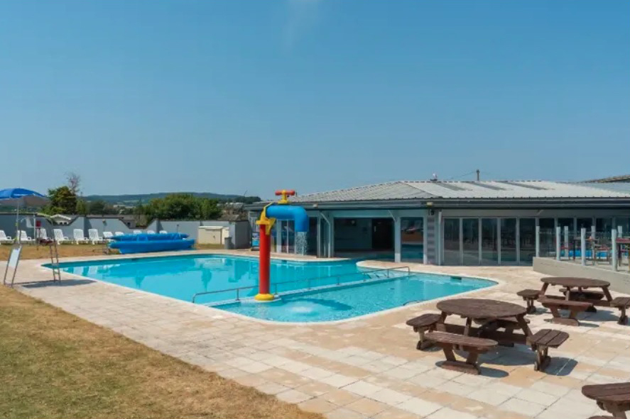 a large swimming pool surrounded by picnic tables and chairs on a sunny day .