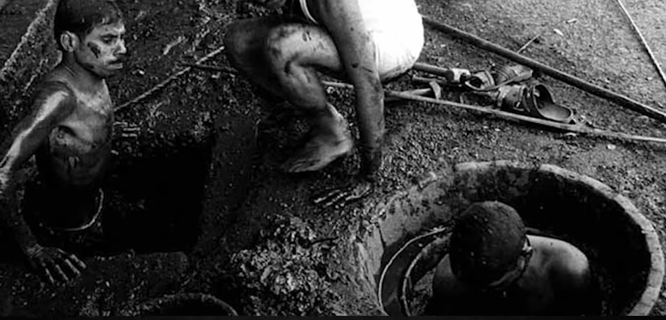 a black and white photo of two men working in a manhole .