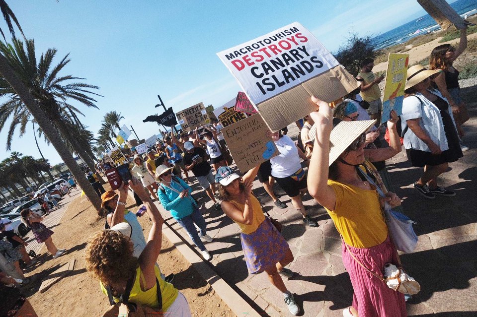 a woman holding a sign that says macrotourism destroys canary islands