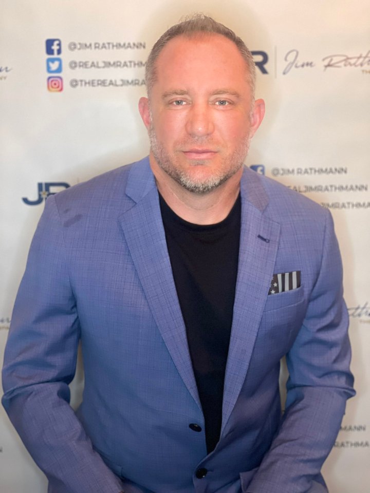 a man in a blue suit stands in front of a wall that says jim rathmann