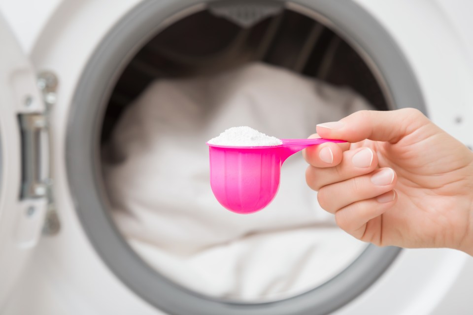 a person is measuring laundry detergent in a pink measuring cup