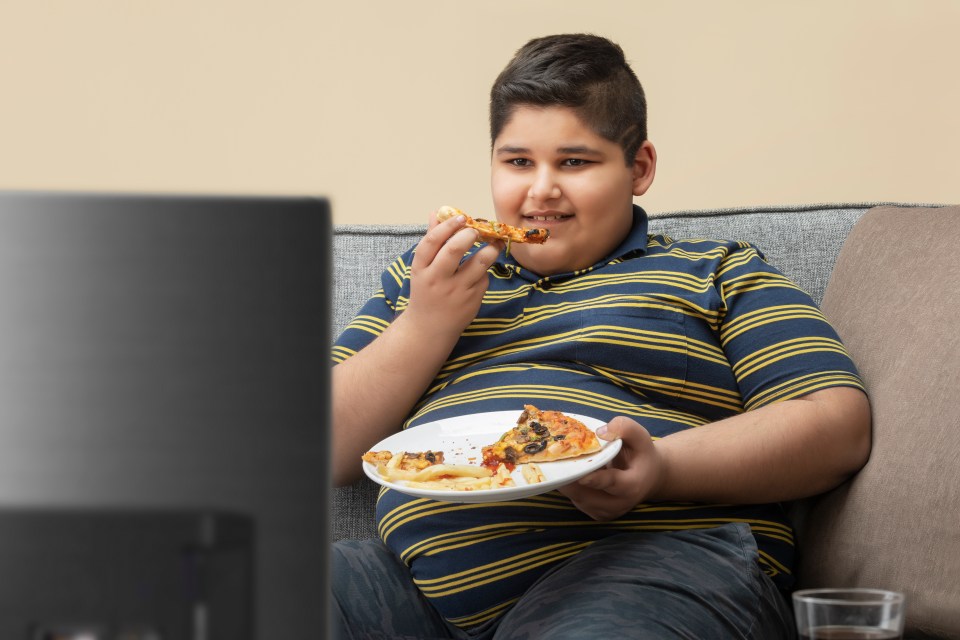 a boy sitting on a couch eating a slice of pizza