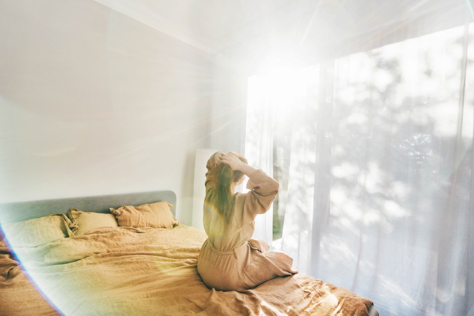 a woman sits on a bed in front of a window