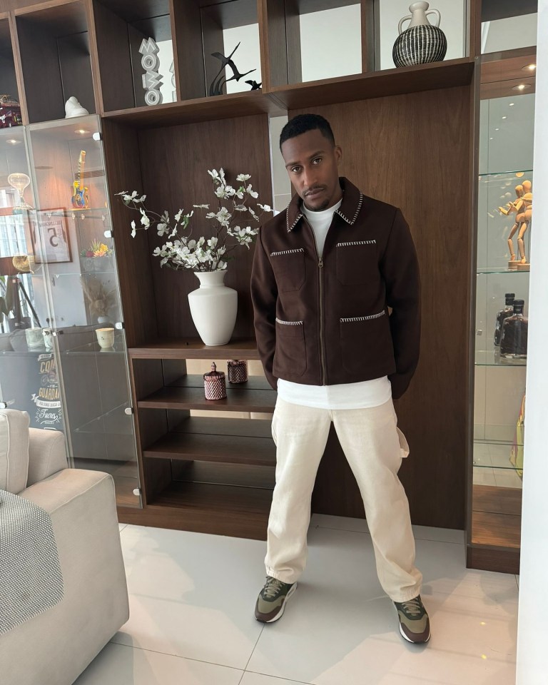 a man in a brown jacket stands in a living room