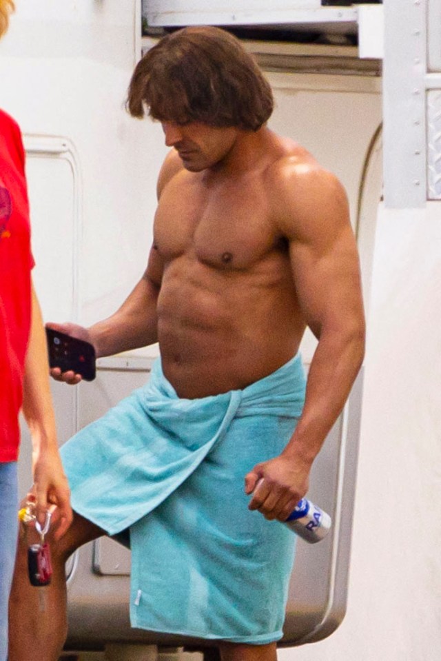 a shirtless man wrapped in a blue towel holds a can of pepsi