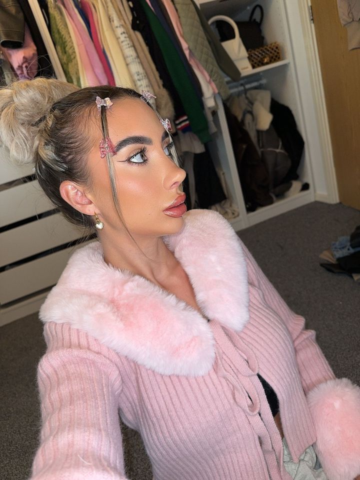 a woman wearing a pink sweater with a fur collar takes a selfie