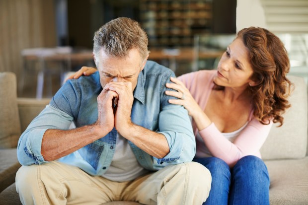 a woman comforts a man who is sitting on a couch