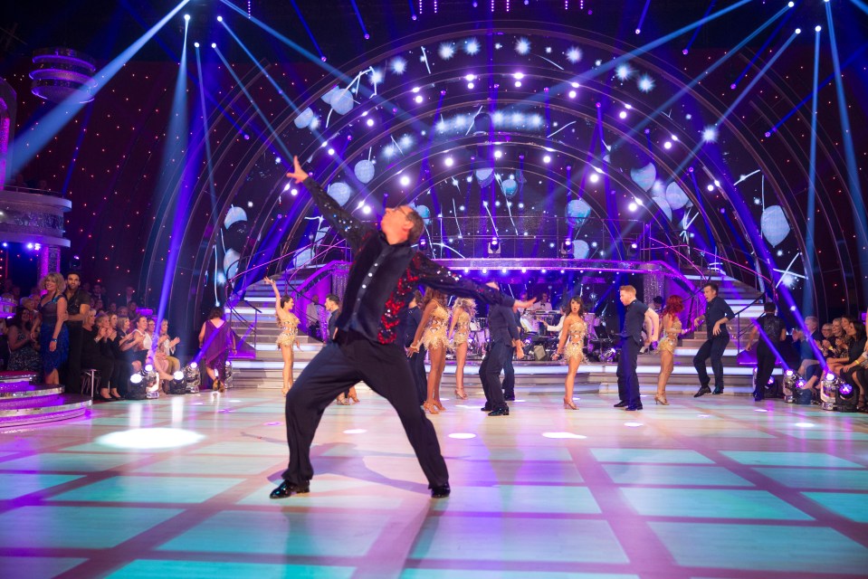 a group of people are dancing on a stage with purple lights