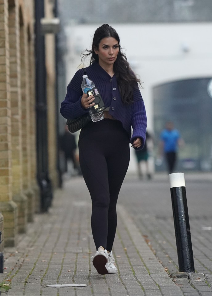 a woman walking down a sidewalk holding a bottle of water