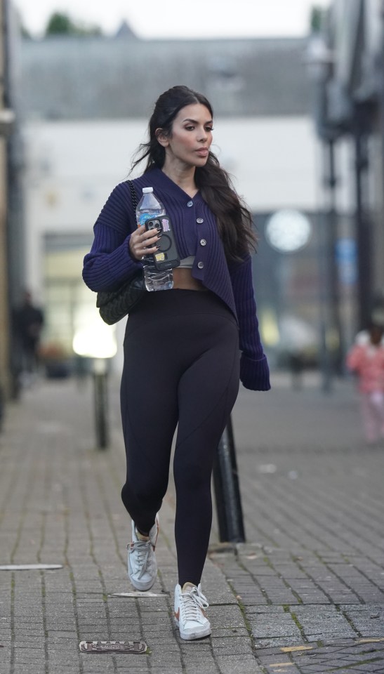 a woman walking down a street holding a bottle of water