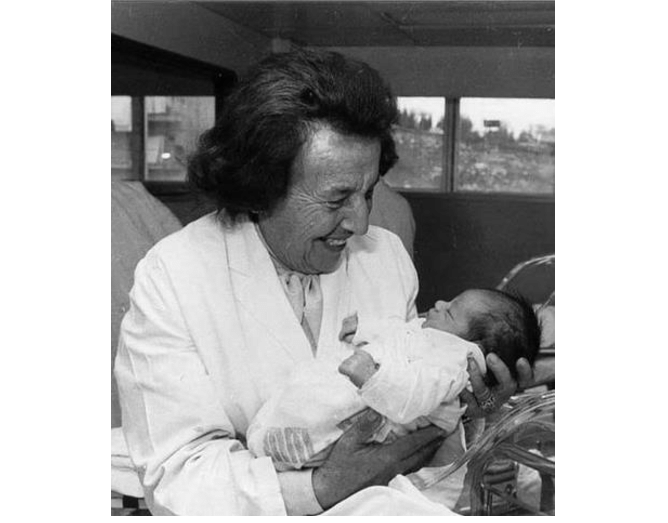 a woman in a lab coat is holding a baby in her arms