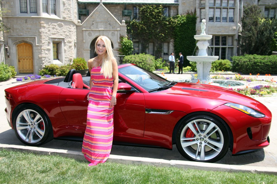 a woman in a pink dress stands next to a red sports car