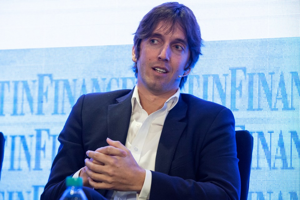 a man in a suit sits in front of a screen that says ' infinia ' on it