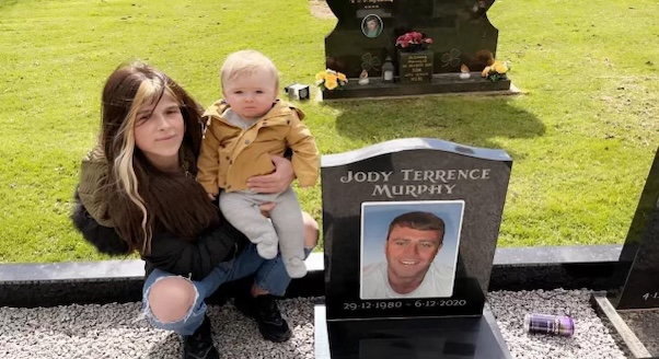 a woman is holding a baby in front of a grave .