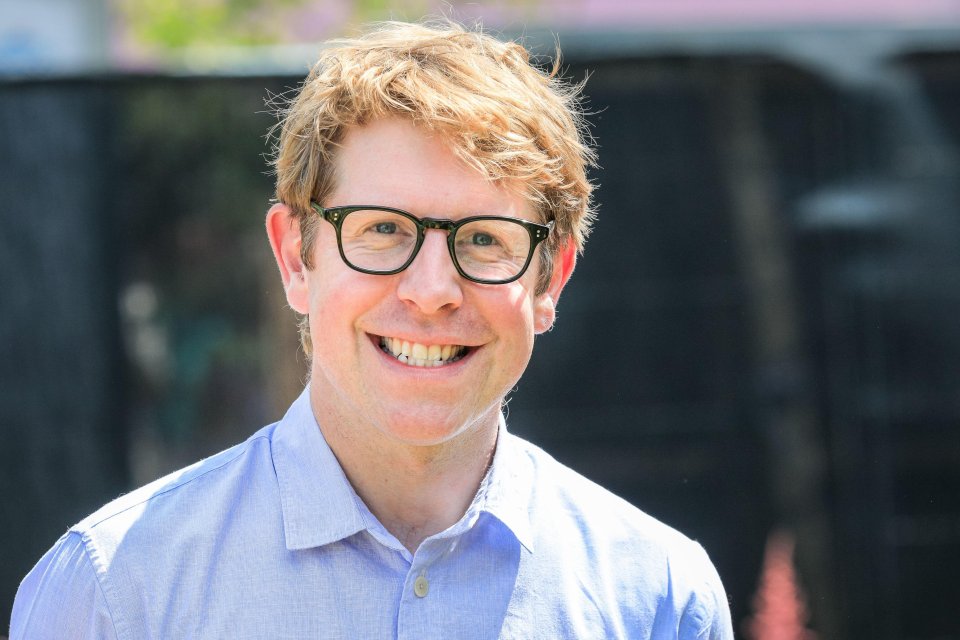 a man wearing glasses and a blue shirt smiles for the camera