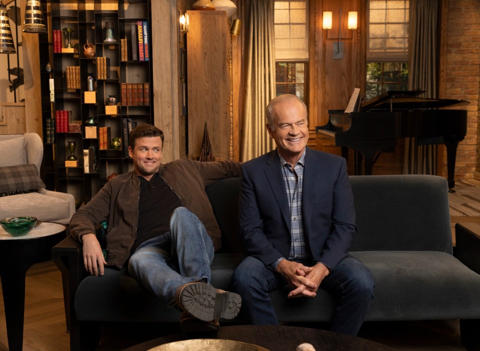 two men sit on a couch in front of a piano