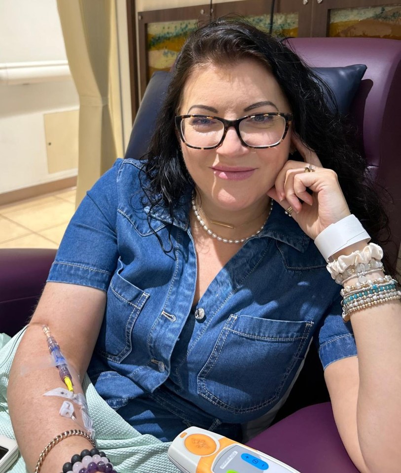 a woman wearing glasses sits in a chair with an iv in her arm