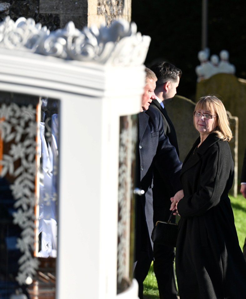 a woman in a black coat stands in front of a white carriage