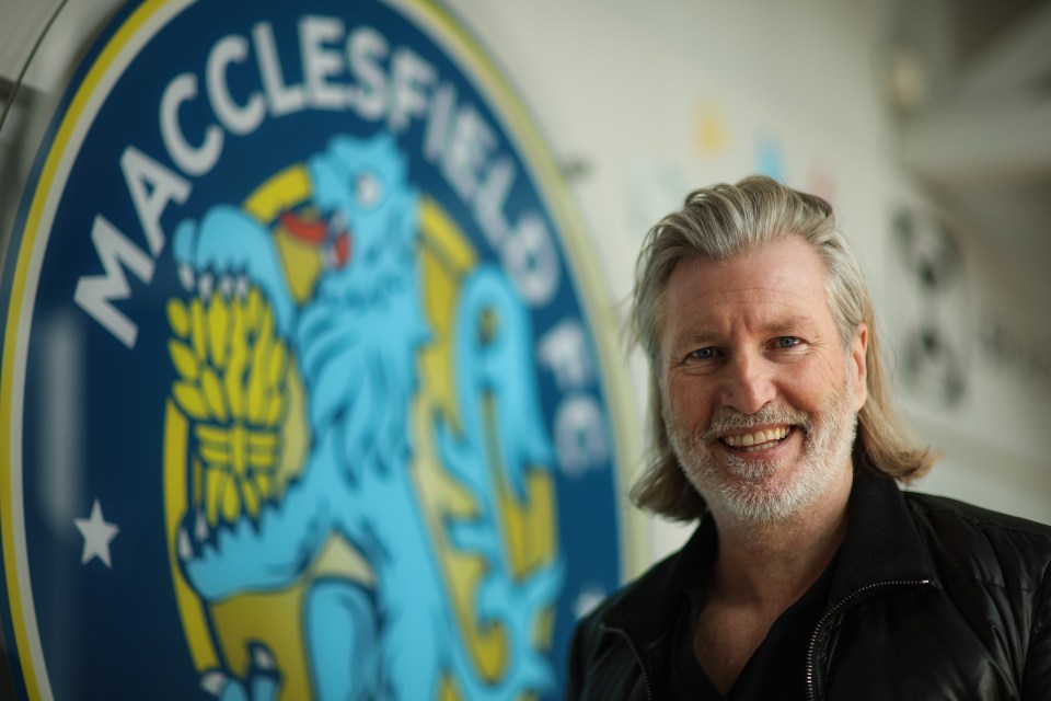 a man stands in front of a macclesfield fc logo