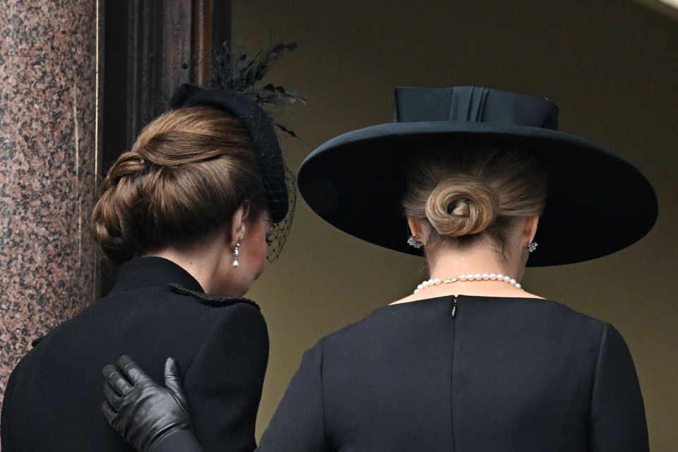 a woman wearing a pearl necklace stands next to another woman wearing a black hat