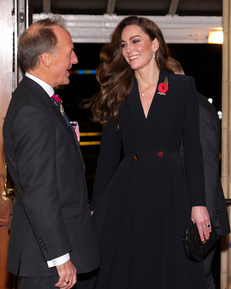 a woman in a black jacket has a poppy pin on her jacket