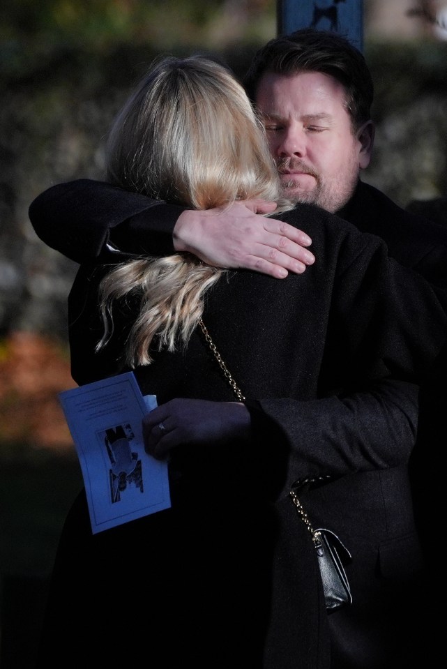 a man in a black coat is hugging a blonde woman