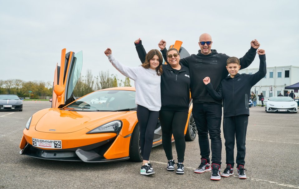 a family stands in front of an orange sports car with a license plate that says supercar