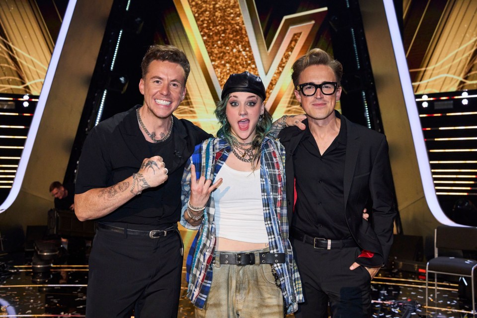 two men and a woman pose for a picture in front of a large letter v