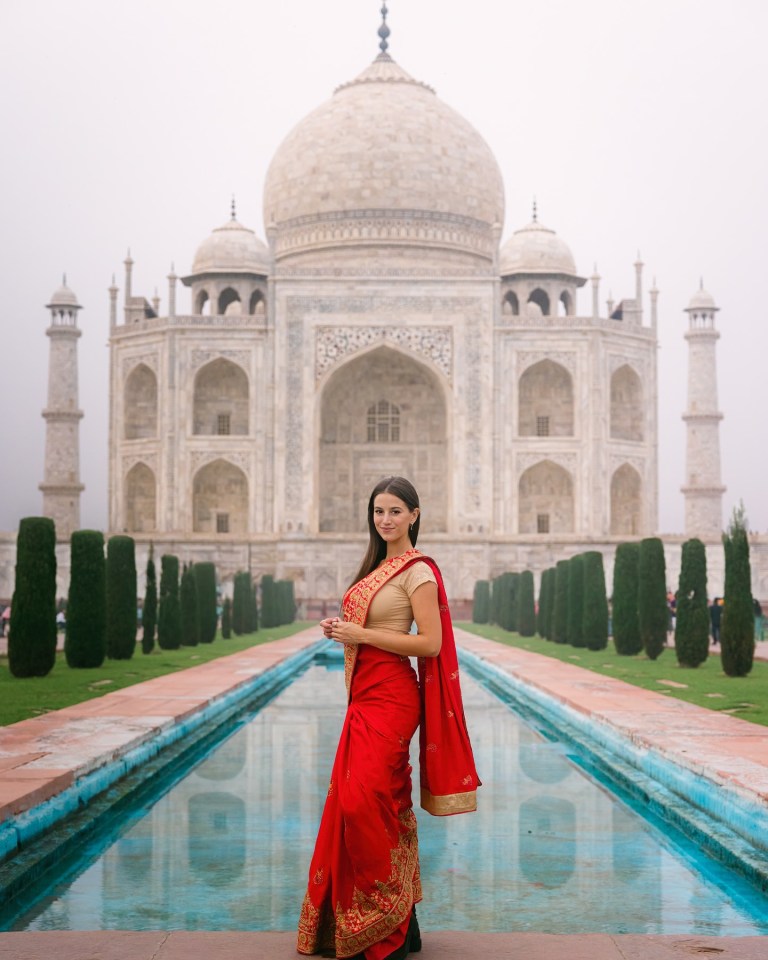 a woman in a red sari stands in front of the taj mahal