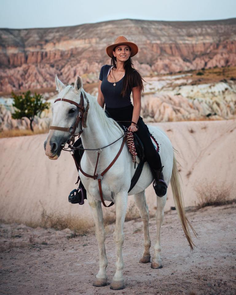 a woman in a hat is riding a white horse