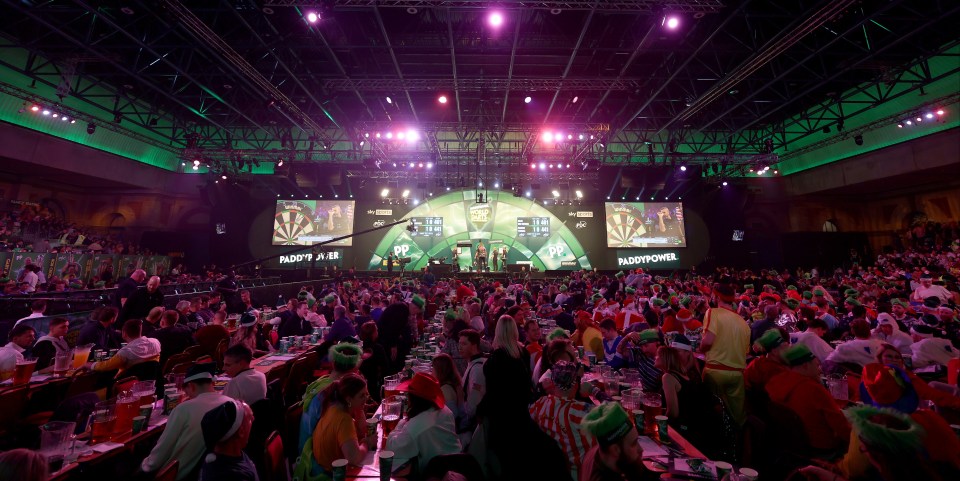 a large crowd of people are watching a darts match