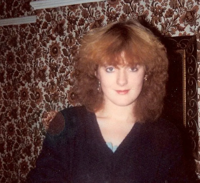 a woman with red hair is standing in front of a floral wallpaper