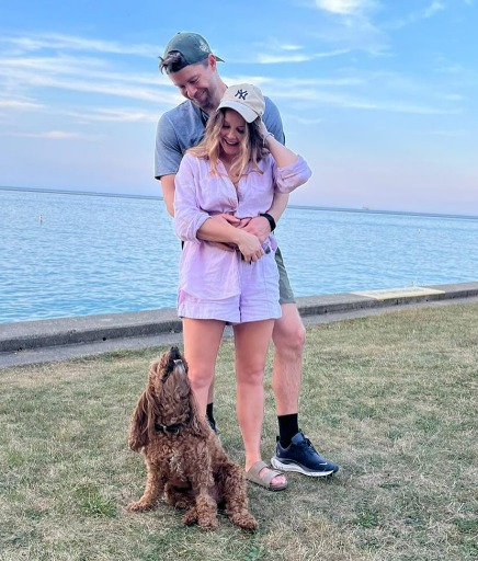 a man wearing a ny hat stands next to a woman and their dog