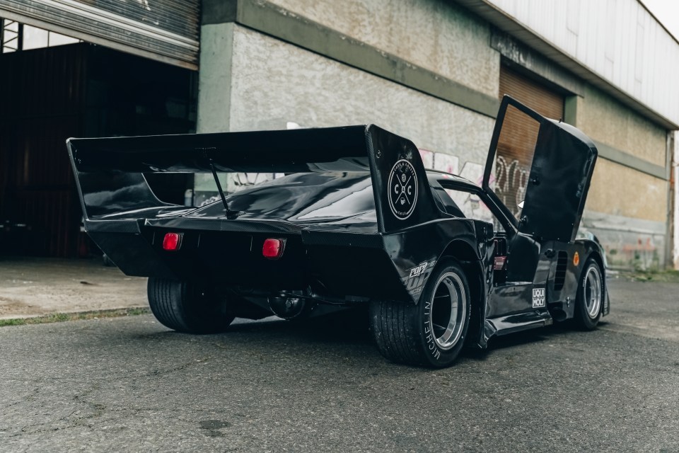 a black sports car with the hood open is parked in front of a building