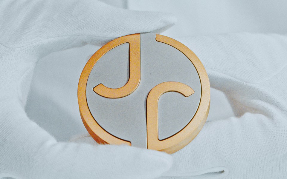 a person wearing white gloves is holding a gold coin with the letter j on it