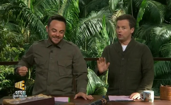 two men are sitting at a table in front of a sign that says live australia