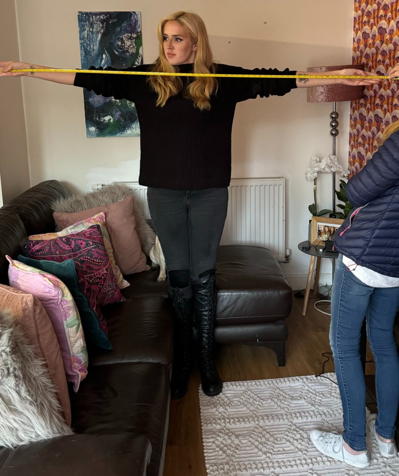 a woman in a black sweater is measuring her arms with a tape measure