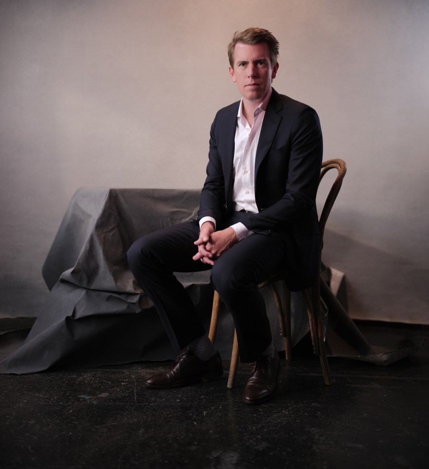 a man in a suit sits in a chair with his hands folded